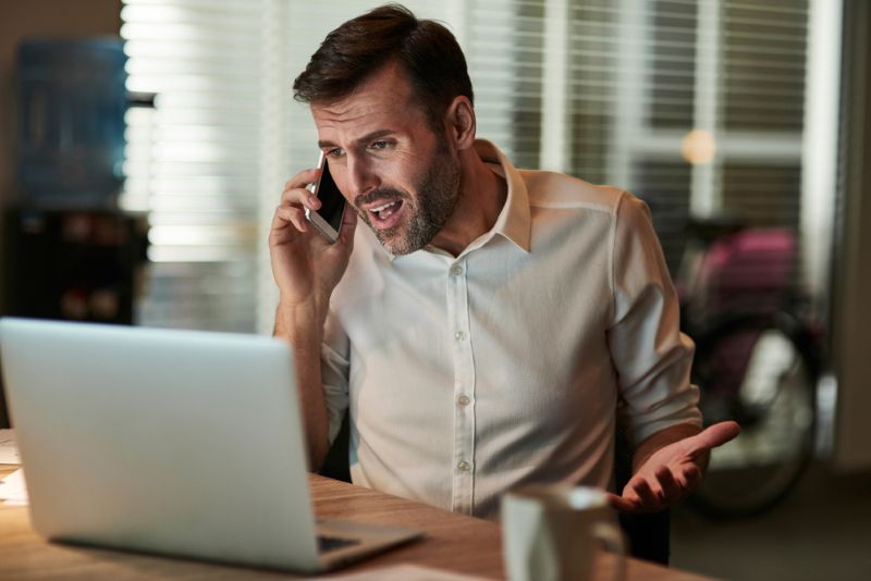 Confused man on a phone call yelling at his laptop