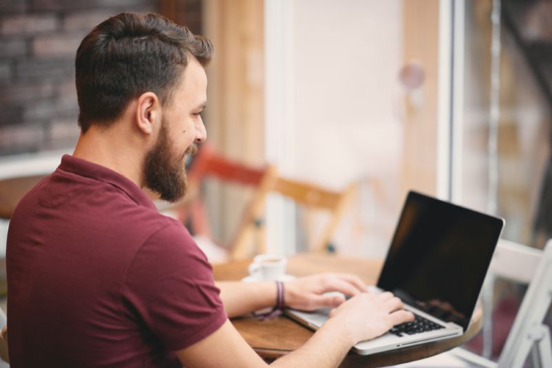 Smiling man working from his laptop in a cafe