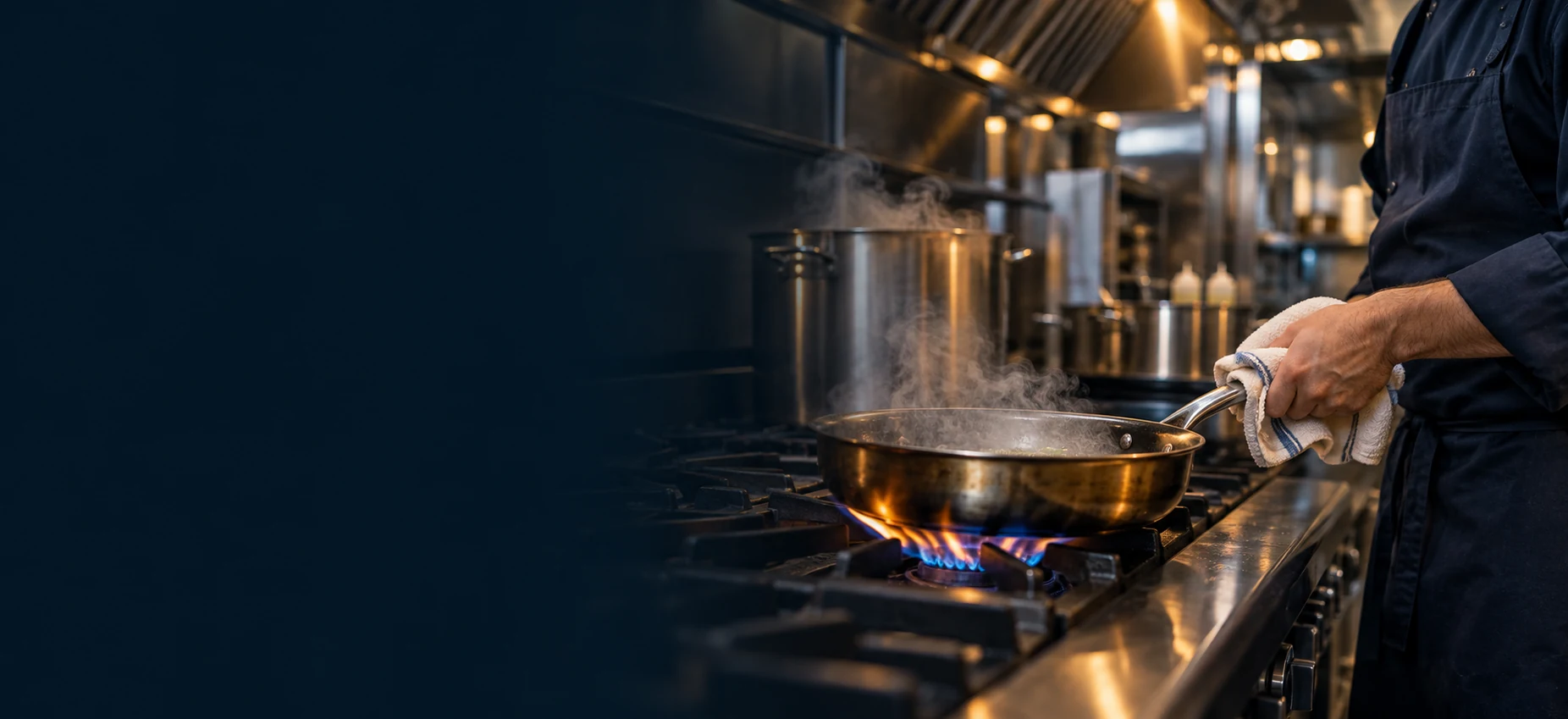 Kitchen worker handling a steaming pan over a gas burner in a commercial kitchen